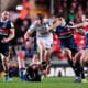 Intense rugby action with players from opposing teams tackling fiercely during a night game.