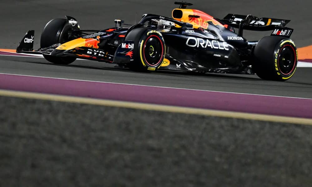 ed Bull Racing Formula One car, painted black with yellow and red accents, races along a track during a night race, with illuminated track boundaries enhancing the high-speed scene.