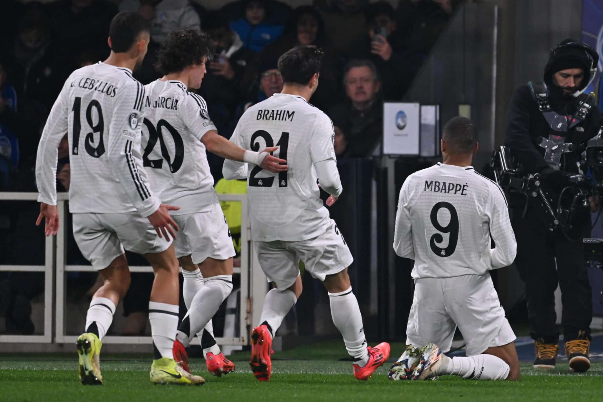 Celebration scene as soccer players rejoice after a goal, featuring Mbappe and his teammates in white kits.