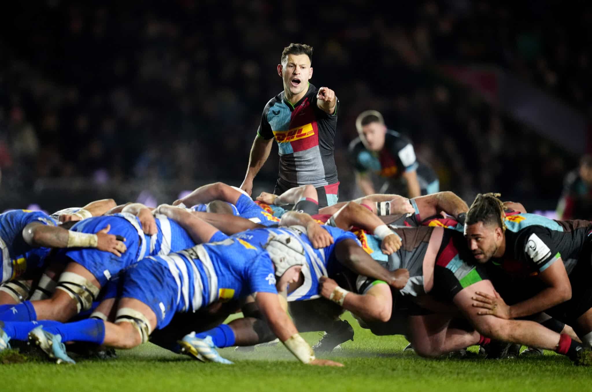 Intense rugby match scene with a scrum half poised to release the ball from the scrum, under the watchful eyes of competitors.