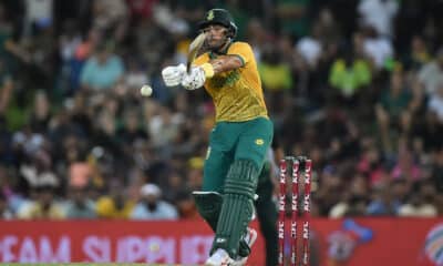 A South African cricketer in action, striking the ball during a night match.