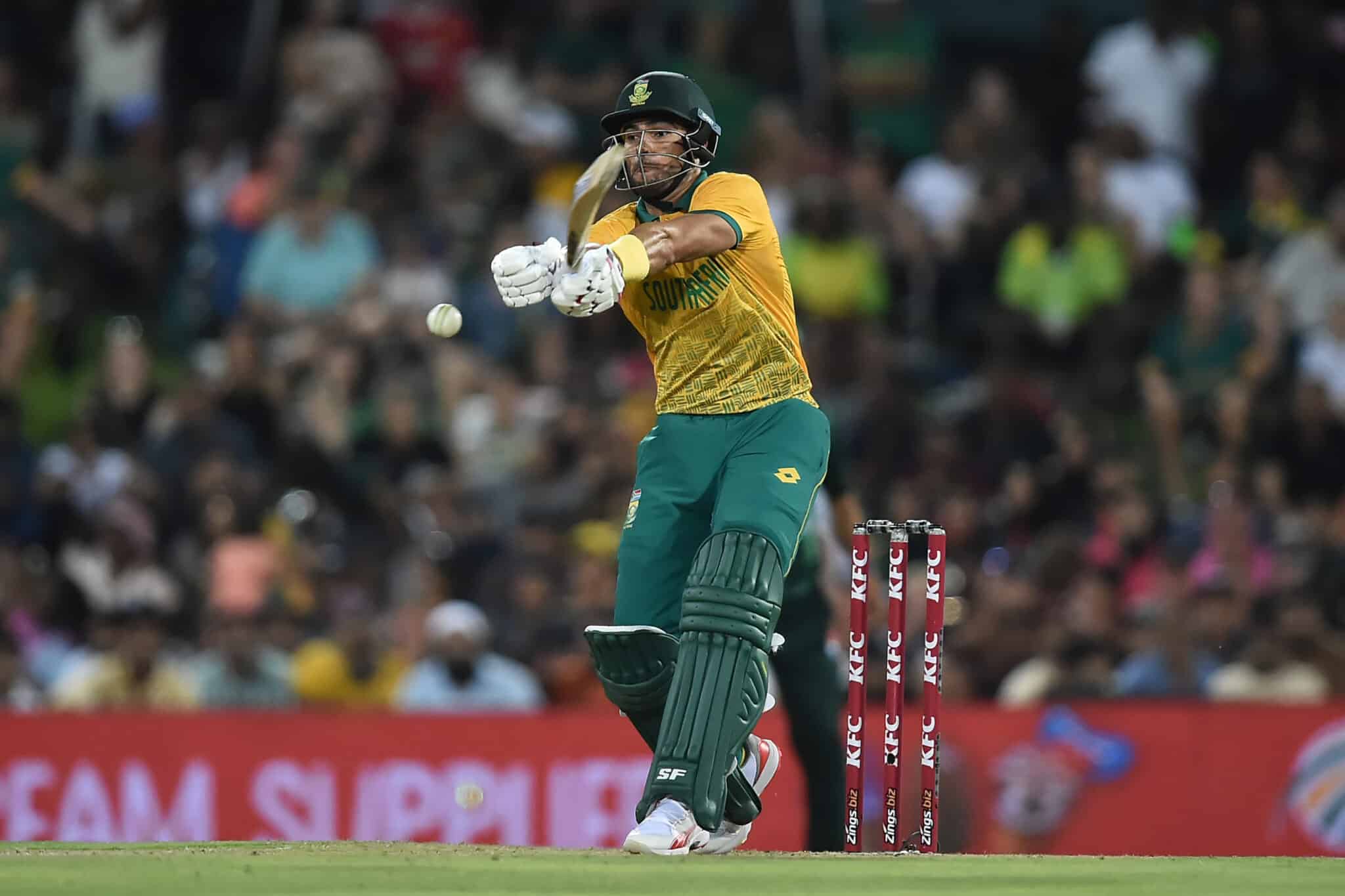 A South African cricketer in action, striking the ball during a night match.